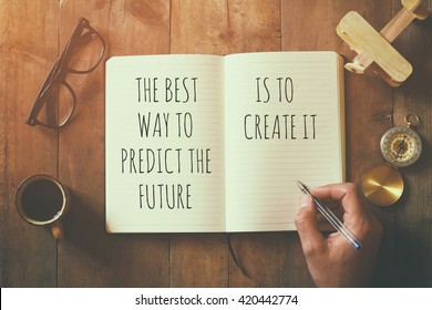 open notebook over wooden table with motivational saying the best way to predict the future is to create it. top view
