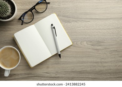 Open notebook, pen, glasses and cup of coffee on wooden table, flat lay. Space for text