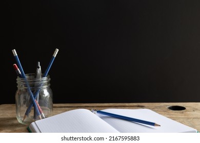 Open notebook with pencil laying on it with a jar of pencils on a vintage wood desk with copy space on a black background  - Powered by Shutterstock