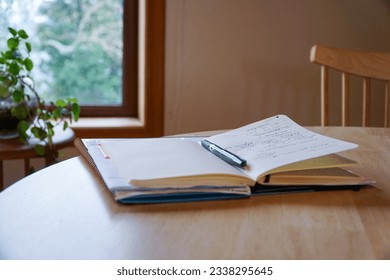 An open notebook with a pencil placed on top, resting on a wooden table inside the house, symbolizing creativity and ideas in a cozy home setting. - Shutterstock ID 2338295645
