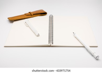 Open notebook with pencil rubber and pencilcase on light grey background
