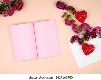 open notebook with pink blank pages and Turkish carnation Dianthus barbatus flower buds and a white paper envelope on a peach background, top view