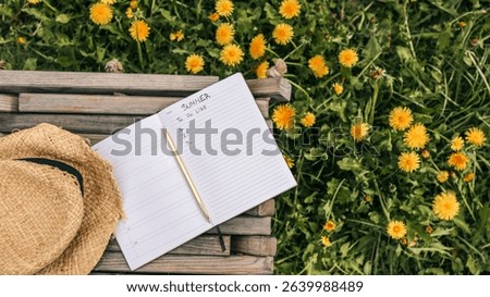 Open notebook with "Summer To Do List" written inside, resting on a wooden bench in a field of blooming dandelions, with a straw hat placed nearby in soft afternoon sunlight.