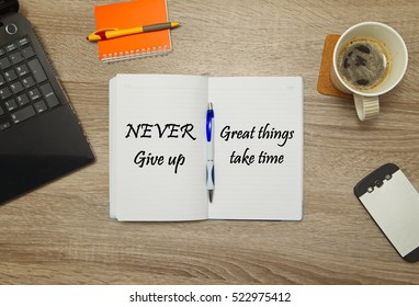 Open notebook with text "Never Give Up - great things take time" and a cup of coffee on wooden background.