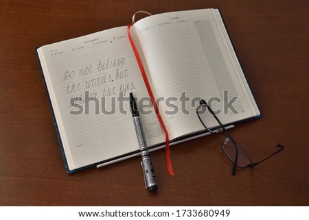 An open notebook with a written proposal, a pen and glasses on the table.