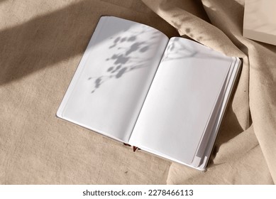 Open notepad blank sheets and floral sunlight shadows on a neutral beige linen background, mock up with copy space, aesthetic writer blog design template