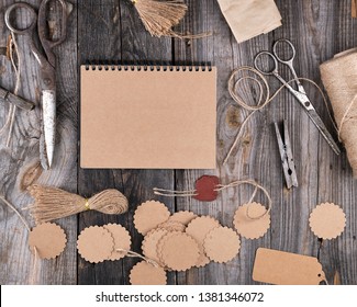 open notepad with brown empty sheets on a gray wooden table, next to it are a rope, paper tags and scissors, top view