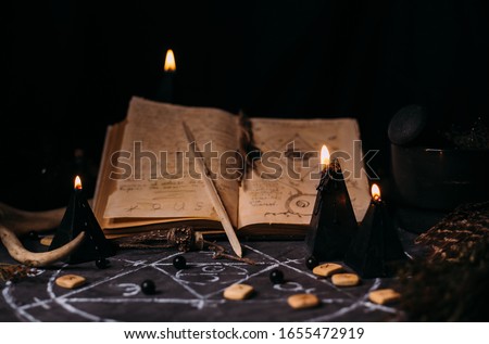 Open old book with magic spells, runes, black candles on witch table. Occult, esoteric, divination, superntural and wicca concept. Halloween vintage background
