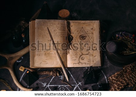 Open old book with magic spells, runes, black candles on witch table. Occult, esoteric, divination and wicca concept. Halloween vintage background