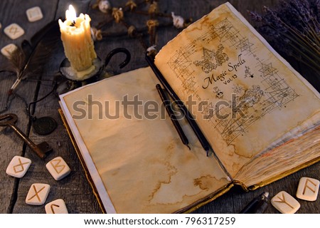 Open old book with magic spells, runes, candle and key on witch table. Occult, esoteric, divination and wicca concept. Halloween vintage background