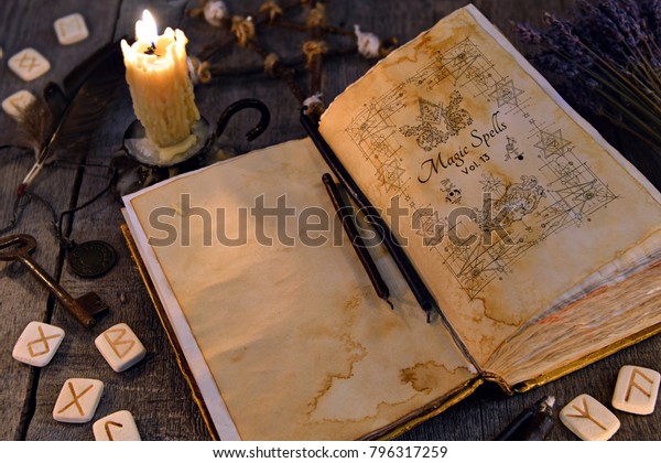 Open old book with magic spells, runes, candle\
and key on witch table. Occult, esoteric, divination and wicca\
concept. Halloween vintage\
background