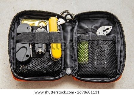 Open orange EDC pouch with multitool, flashlight, lighter, and other survival gear. Everyday carry organizer