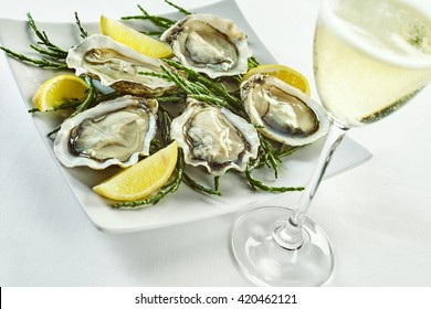 Open oyster shells with lemon wedges in plate with curled edges and drink in tall champagne glass over white