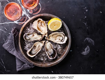Open Oysters on metal plate and rose wine on dark marble background 