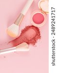 An open pack of pink blush, a sample of the blush texture and two makeup brushes on a pink vertical background. top view.