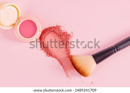 An open pack of pink blush, a sample of the blush texture and makeup brush on a pink background. top view. Beauty and care concept