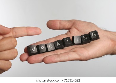 Open palm with eight computer buttons with word UPDATING and pointing finger - Shutterstock ID 715314022
