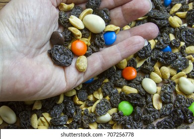 Open Palm Of Hand Holdng Trail Mix With Raisins, Chocolate Pieces And Peanuts.