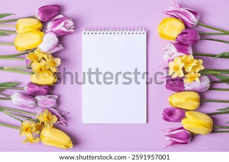 Open paper notebook with empty page with purple and yellow tulips and yellow daffodils on purple background. Top view, flat lay, work space on purple background.