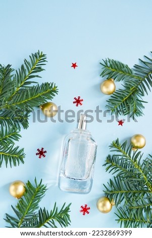 Open perfume bottle with new year tree branches, snowflakes, small hearts on the blue background. Christmas perfume gift idea. Winter holiday celebration perfume composition. Empty place for text.