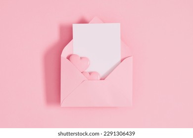Open pink envelope with paper card and heart on pastel pink table background. Birthday, Wedding, Mother's Day, Valentine's day, Women's Day. Flat lay, top view, copy space