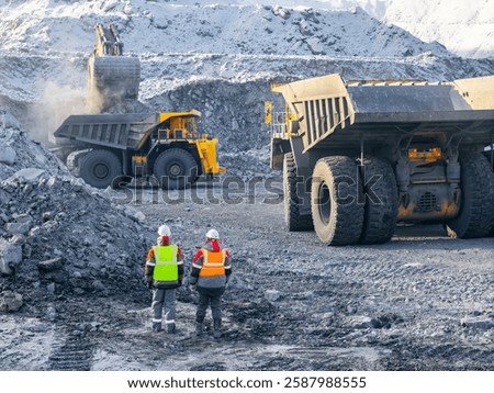 Open pit coal mining with two male workers in high visibility gear, aerial top view.