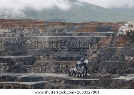 Open pit mine simultaneous blasts along terraced rock benches, gold and copper ore mining.