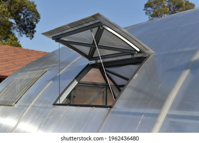 Open polycarbonate greenhouse window with bright sun and clear blue sky and trees in the background. Too hot.