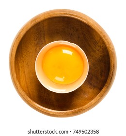 Open Raw Chicken Egg With Yolk And White In Its Shell In A Wooden Bowl. Common Food And Versatile Ingredient Used In Cooking. Isolated Macro Food Photo Close Up From Above On White Background.