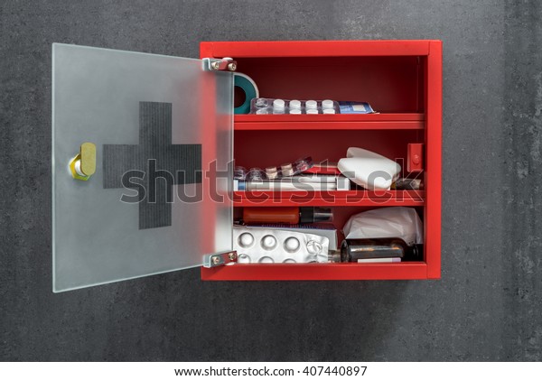 Open red metal\
medicine cabinet full of drugs hanging on a dark gray marble wall\
background. Front view