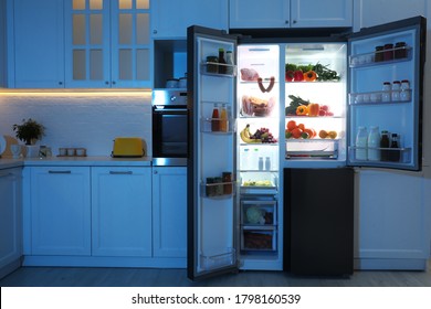 Open Refrigerator Filled With Food In Kitchen At Night