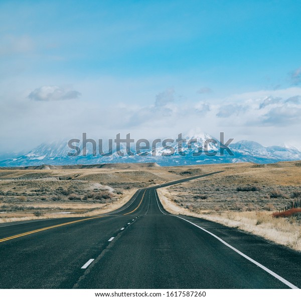 An open road ahead, leading towards the mountains. The\
sides of the road are barren, drawing the viewer toward the path\
ahead. 