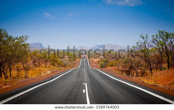 The open road in\
Kimberly, Western Australia. Straight single lane asphalt road\
stretching into the distance with mountains in the background.\
Holiday adventure.\

