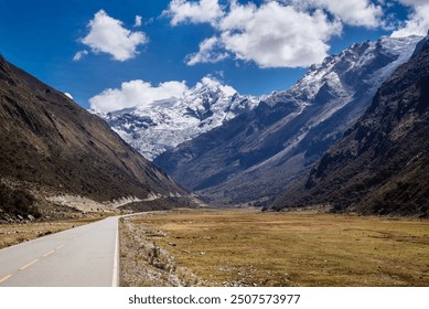 An open road stretches through the vast valley of the Peruvian Andes, with snow-capped mountains towering in the background under a clear blue sky, epitomizing the raw beauty of nature. - Powered by Shutterstock