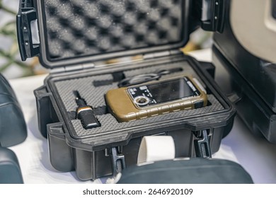 Open rugged case containing a black device with multiple lenses and protective cover, possibly a smartphone or camera, beside it are a lens cap and potential additional lens or filter Placed on patt