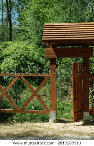 Open rustic wooden gate with a small wooden roof and fence leading into a lush green forest. Vertical shot of an open wooden entrance door with a wooden shingle roof and cross-lattice fence set against a sunlit woodland background.

Wersja koncepcyjna (zaproszenie, wejście, przejście):
