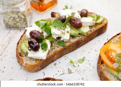 Open sandwich made of slices of sourdough bread with avocado, feta cheese, kalamata olives, olive oil and oregano on a wooden white table, close-up. Vegetarian food - Powered by Shutterstock