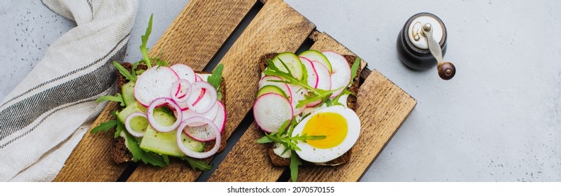 Open sandwiches on dark rye bread with eggs, shrimps, radishes, cucumber, cream cheese and arugula for breakfast on old dark background. Smorrebrod Traditional dish of Danish cuisine. Top view.