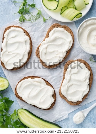 Open sandwiches, rye bread bruschetta with cream cheese spread (ricotta) and cucumber slices on white wax paper. Healthy delicious breakfast, lunch or snack food. Top view. Blue background.