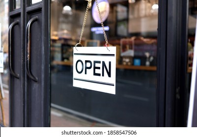 An Open Sign Hanging On The Black Metal Frame Glass Door In Front Of The Cafe And Coffee Shop. Sign Open Now Concept.