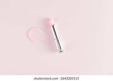 Open silver packaging of fruit flavored balm or lipstick on a pink background with a sample of the texture of the balm stroke. top view. Presentation