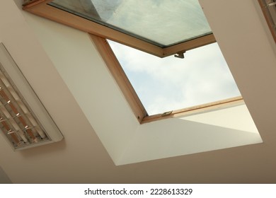 Open skylight roof window on slanted ceiling in attic room, low angle view