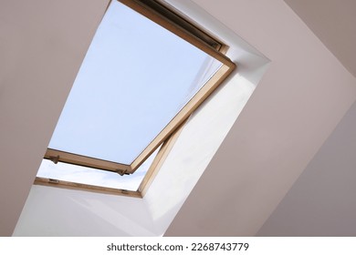Open skylight roof window on slanted ceiling in attic room