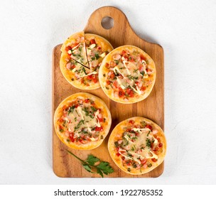Open small pies, mini pizzas with sausage, pickles, tomatoes, mozzarella, parsley on a wooden board on a light background top view