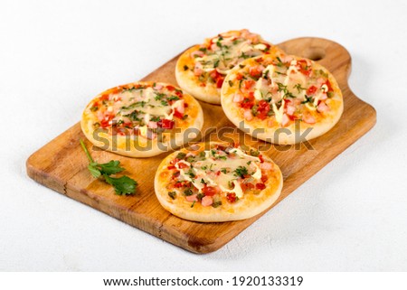 Open small pies, mini pizzas with sausage, pickles, tomatoes, mozzarella, parsley, greens on a wooden board on a white background 