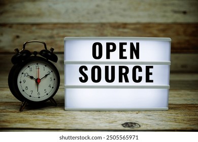 Open Source text on LED lightbox with alarm clock on wooden background
