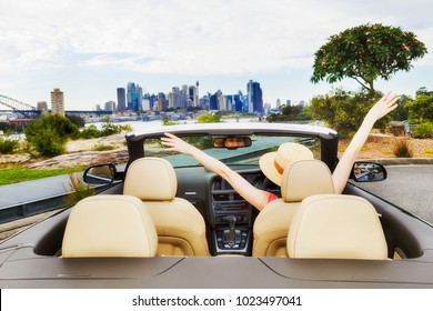 Open Space In Modern Luxury Passenger Sports Car With Soft Top Down And Happy Lady Driver Enjoying Wealthy And Healthy Lifestyle In View Of Sydney City CBD.