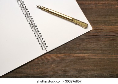 An Open Spiral Bound Notebook With White Pages And Gold Fountain Pen On The Rough Rustic Wood Table. Overhead View - Powered by Shutterstock