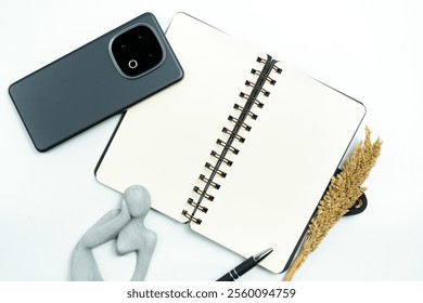 An open spiral notebook, smartphone, and black pen arranged on a white desk with decorative wheat. Ideal composition for themes of organization, productivity, or creative writing in a workspace. - Powered by Shutterstock