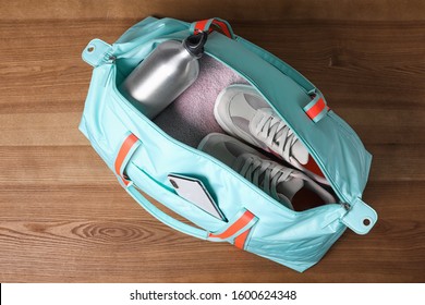 Open Sports Bag Full Of Gym Stuff On Wooden Background, Top View